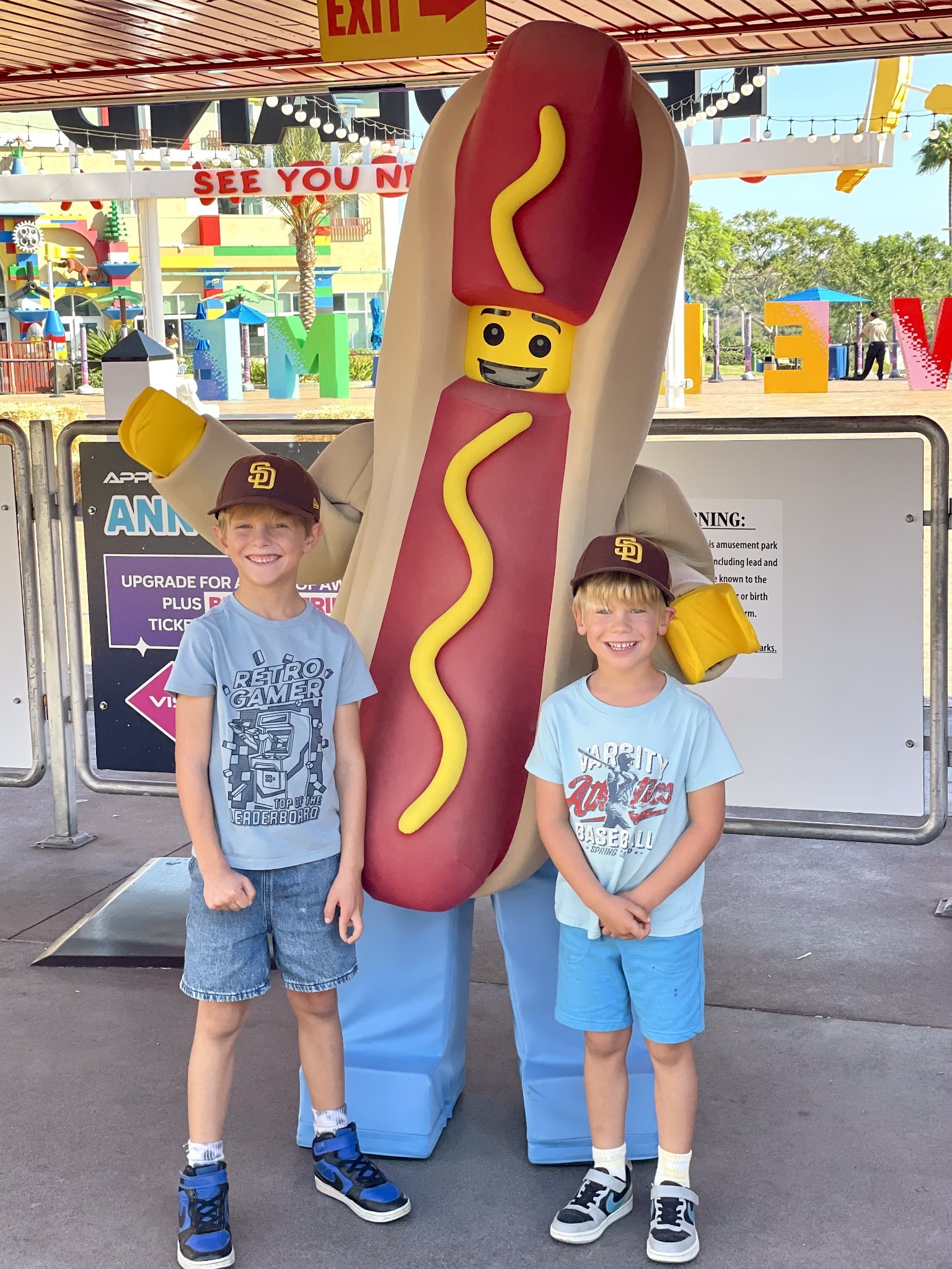 Two boys smiling beside a LEGO hot dog character