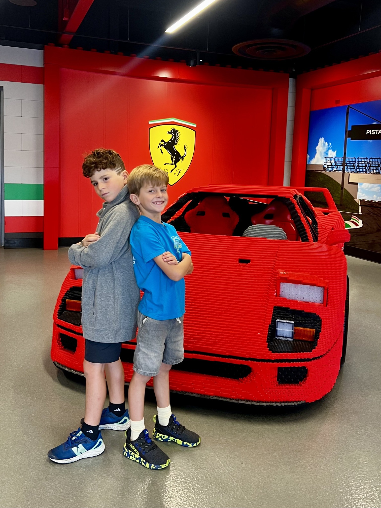 Two boys posing beside a red LEGO Ferrari