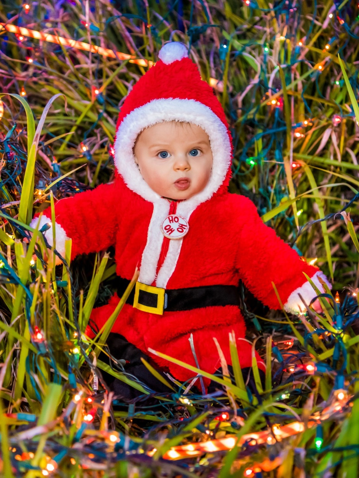 A baby in a Santa outfit among colorful lights